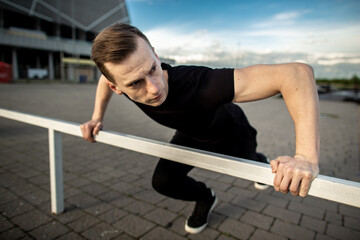 Fototapeta premium Young man doing push ups on horizontal bar outdoors. Man training near the stadium. Fitness, sport, exercising and lifestyle concept