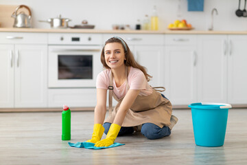 Full length portrait of happy young housewife washing floor at kitchen