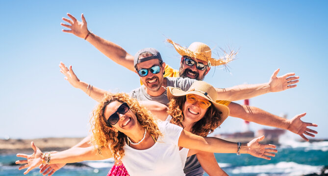 Group of happy adult friends enjoy and celebrate together the summer holiday vacation travel leisure acitivity - men and women smiling and having fun with ocean in background - joyful couples