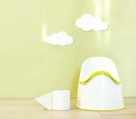 A baby potty in the nursery with decorative clouds and a roll of toilet paper.