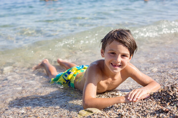 Sweet child, preteen boy, lying on the beach in France on sunset