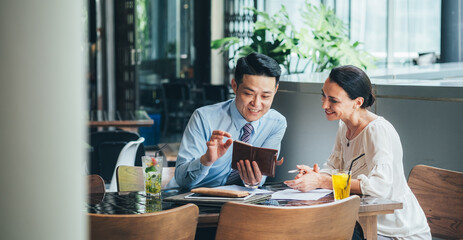 Smiling business people looking in mobile phone and laughing together. Businessman showing his smartphone to female colleague and explaining something while sitting in modern cafe