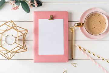Top view of white working table background with blank paper notebook, cup of coffee. Flat lay green...
