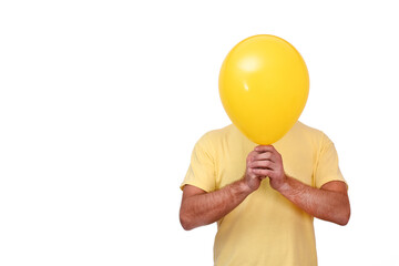 A man holds a balloon covering his face. Yellow ball covering the face. The male covers his face...