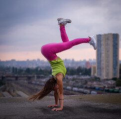Flexible girl keep balance on hands on the cityscape background . Concept of creativity, balance...