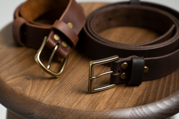 Two brown leather men's belts with bronze clasp on wooden chair with a white background. Handmade leather belt.
