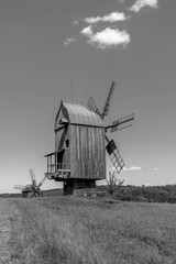 Old wodden windmill on a green meadow, field. Blue sky with white clouds. Old photo. Black and white photo.