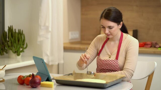 Female chef preparing a pizza and watching recipes online on platform for watching videos on your tablet.