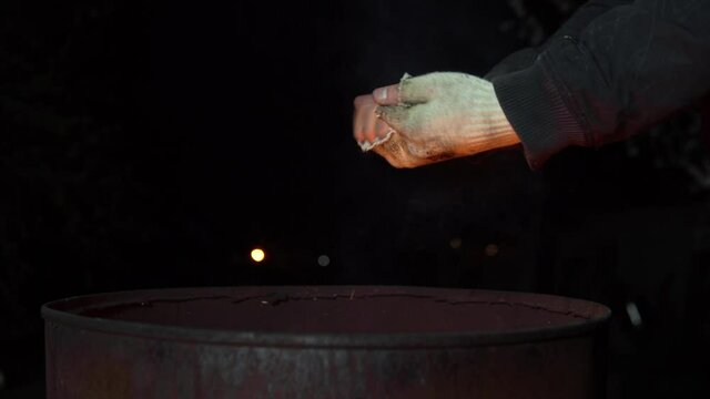 A homeless man warms his hands at night near a barrel of fire. Hands close up.