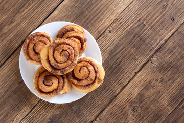Cinnabon buns. Freshly baked cinnamon roll with spices and cocoa filling and coffee or cappuccino on white serving plate on wooden background with copy space. Swedish breakfast.