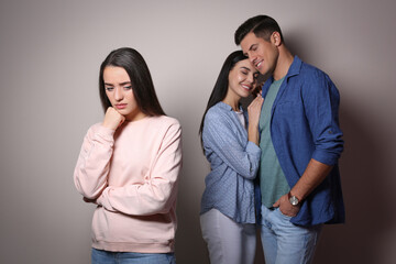 Unhappy woman feeling jealous while couple spending time together on grey background