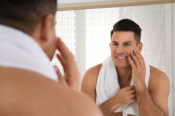 Handsome man with towel near mirror in bathroom