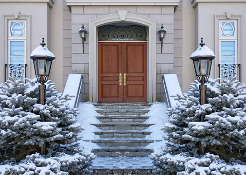 Elegant Wood Grain Front Door Of House In Winter With Snow Covered Pine Bushes