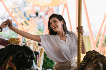 The asian young woman happily smiling and sitting in the carousel of the amusement park