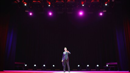 Showman. Young male entertainer, presenter or actor on stage. Back, arms to sides, smoke on...