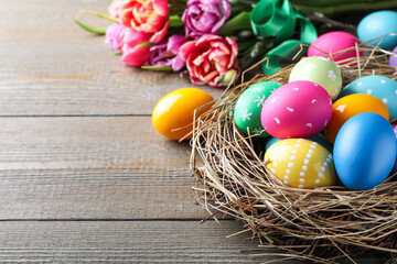 Bright painted eggs and spring tulips on wooden table, closeup view with space for text. Happy Easter