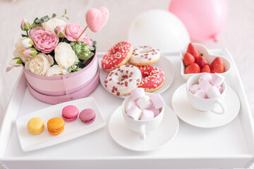 Flowers and sweets on white table and balloons on the white bed. Gift for Valentine's day or March 8 or Mother's Day or birthday