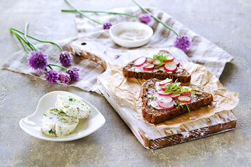 Open sandwiches on triangular rye bread with herbal butter and chopped fresh radish on a wooden board