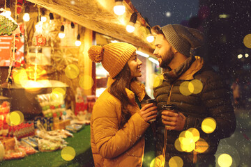 Lovely couple with cups of hot drinks spending time together at Christmas fair