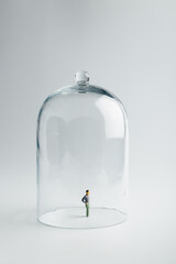 Small figurine in quarantine under a glass dome on a bright background with copy space.