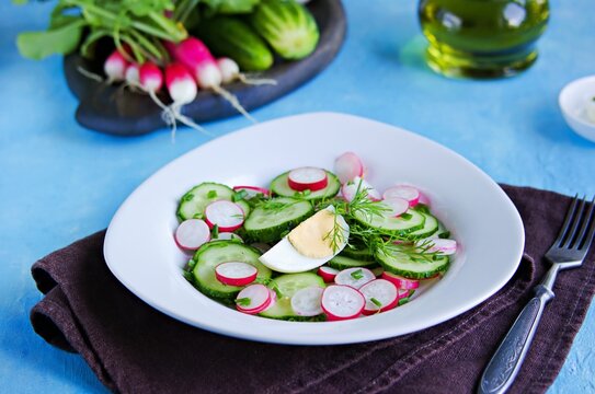 Summer salad with radish, cucumber and boiled egg in a white plate on a blue concrete background. Vegetable salads.