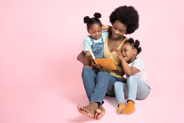 Family reading concept. Two adorable small african girls kids in colorful clothes, listening their...