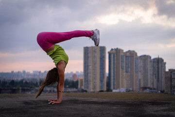 Flexible girl keep balance on hands on the cityscape background . Concept of creativity, balance...