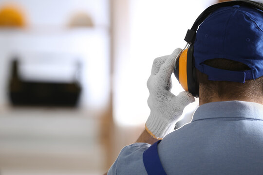 Worker wearing safety headphones indoors, back view with space for text. Hearing protection device