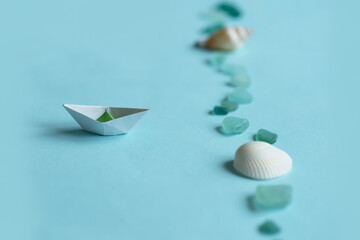 Paper ship, sea shell and stones isolated on blue background. Sea and vacation concept.