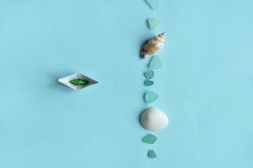 Paper ship, sea shell and stones isolated on blue background. Sea and vacation concept.