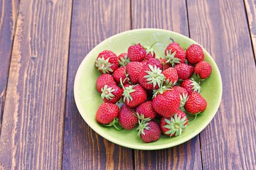 Fresh sweet organic strawberries in a green plate on a wooden background. Harvest strawberries.