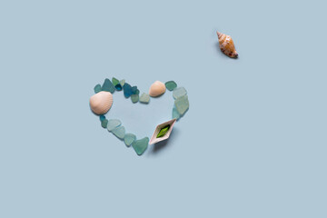 Paper ship, sea shell and stones isolated on blue background. Sea and vacation concept.