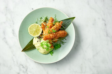 Tasty shrimp fries, breaded with white sauce, green tobiko caviar and lime filed in a green plate on a marble background. Prawn in Asian style. Restaurant seafood