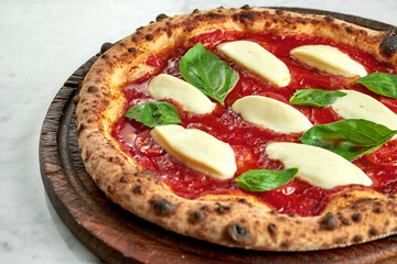 Juicy pizza margarita with red sauce, tomatoes, creamy mozzarella and basil. Italian pizza from wood oven on wood board on marble background