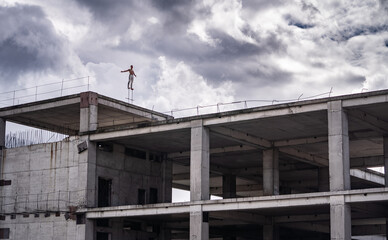 Fototapeta na wymiar Man standing on the edge of rooftop unfinished building with dramatic clouds on background. Concept of confidence, bravery and individuality.