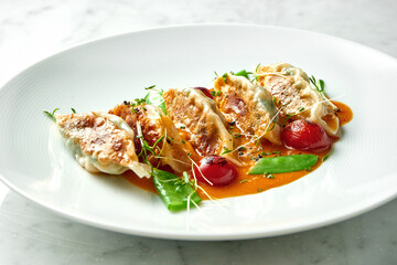 Fried dumplings or Japanese Gyoza in yellow sauce, cherry tomatoes and green peas, served in a white plate on a marble background. Pan-Asian cuisine. Restaurant food