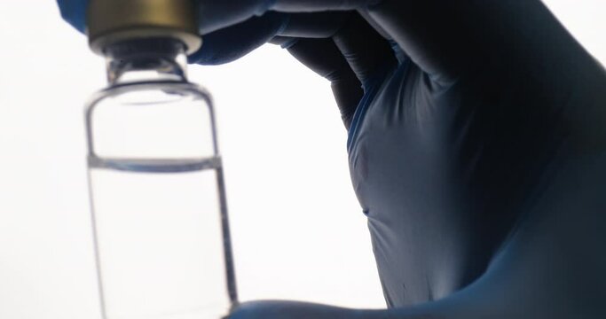 Close up of medical nurse or doctor hand in safety gloves holds a syringe and vaccine bottle. Doctor uses hypodermic needle and a syringe to put a shot of drug as treatment. Health medical concepts.
