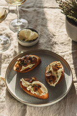 Obraz na płótnie Canvas Bruschettas or toasts with cheese and fried mushrooms with thyme served with glasses of wine on greige linen tablecloth