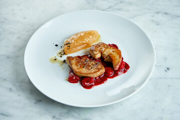 French cuisine dish - grilled foie gras liver with berry sauce and apple puree, served in a white plate on a marble background
