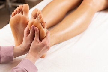 Professional feet massage session close-up. Hands of female massage therapist massaging foot of a young caucasian lady in spa salon. Body care, massage, spa concept.