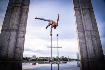 Flexible acrobat doing handstand on the cityscape background with columns on sides. Concept of...