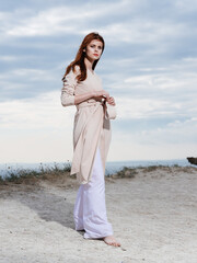 Woman in a sweater and in white trousers on the sand blue sky clouds nature.