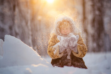 little girl in a fur coat playing with snow