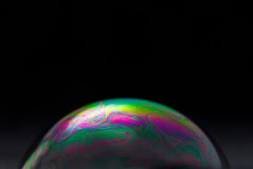 Rainbow soap bubble on a black background. Close-up of a colorful surface.