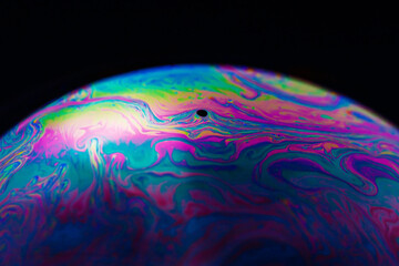 Rainbow soap bubble on a black background. Close-up of a colorful surface.