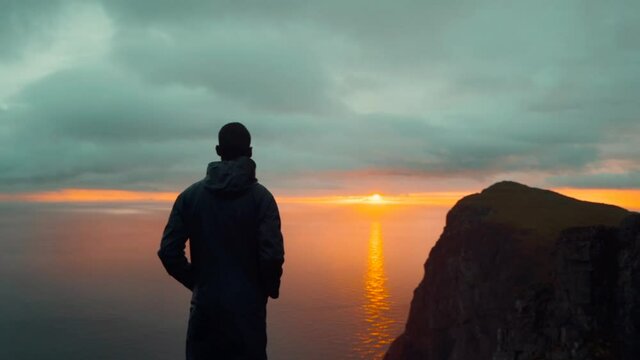 SLOW MOTION: man standing on edge on top of mountain during sunset in Lofoten Islands, Norway