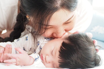 Asian mother kissing her cute newborn baby sleeping in the bedroom at home with love and care Mother and child lifestyle concept
