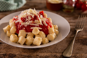 gnocchi with marinara sauce and grated cheese on a white plate and rustic wood
