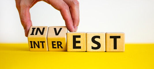 Invest or interest symbol. Businessman turns wooden cubes and changes the word 'invest' to 'interest'. Beautiful yellow table, white background, copy space. Business and invest or interest concept.