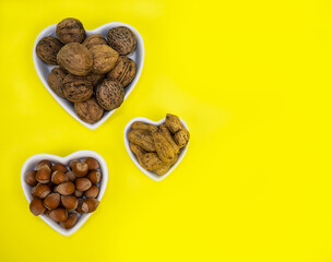 Walnut, hazelnuts and peanuts on a yellow background in a white plate in the shape of a heart. Food.